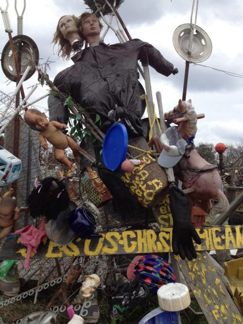 A chaotic assemblage of dolls, mannequins, and various objects hanging on a fence, creating an eerie display.
