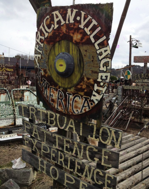 Sign for "African Village in America" with words like "Tribulation," "Patience," "Experience," and "Hope" displayed.
