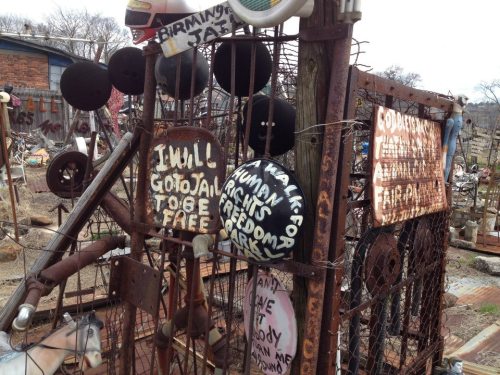 A colorful, eclectic outdoor art installation featuring metal signs and sculptures with various messages and designs.