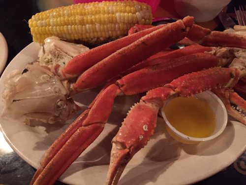 A plate of crab legs with a side of melted butter and a cob of corn.