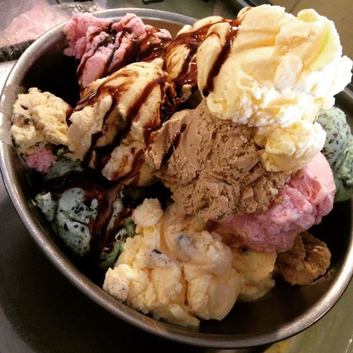 A bowl filled with various colorful ice cream scoops drizzled with chocolate sauce.