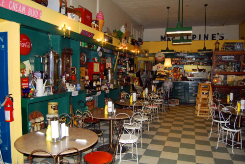 A vintage-style diner with colorful decor, tables, and a nostalgic ice cream counter filled with memorabilia.