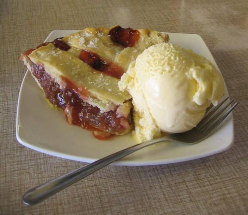 A slice of cherry pie with a lattice crust served on a plate alongside a scoop of vanilla ice cream.