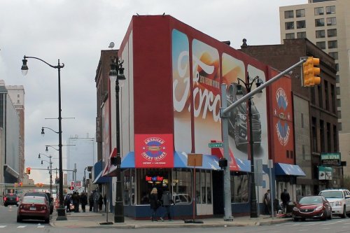 A colorful building with murals, located at a busy street corner, featuring pedestrians and parked cars.