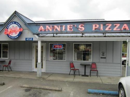 Exterior of Annie's Pizza, featuring a neon "OPEN" sign and outdoor seating.