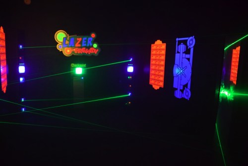 A dark room with colorful laser beams, neon signs, and a checkpoint for a laser tag game.