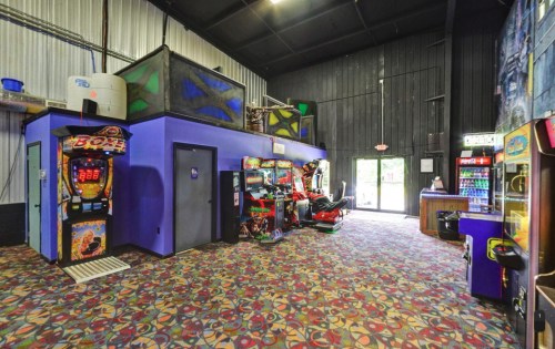 Interior of an arcade featuring colorful game machines, a snack area, and patterned carpet. Brightly lit and spacious.