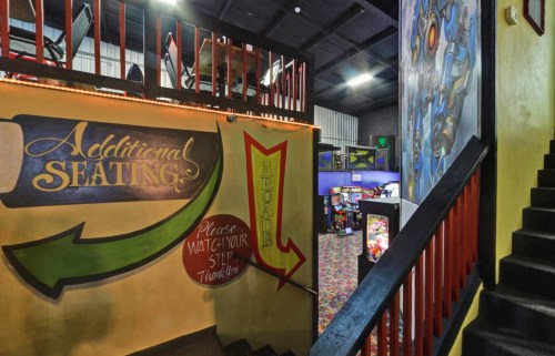Colorful interior of a venue with stairs leading to additional seating and an arcade, featuring vibrant wall art.