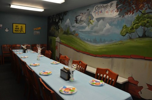 A long table set with plates and decorations in a colorful room featuring a mural of a landscape.
