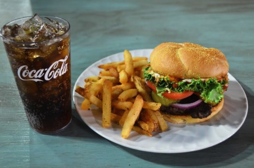 A plate with a burger topped with lettuce, tomato, and onion, served with fries and a glass of cola.