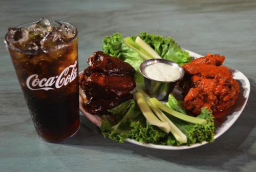 A plate of chicken wings with celery and lettuce, accompanied by a cup of Coca-Cola.