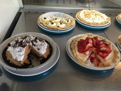 Two pies on a display: one with a chocolate crust and whipped cream, the other topped with strawberries and cream.