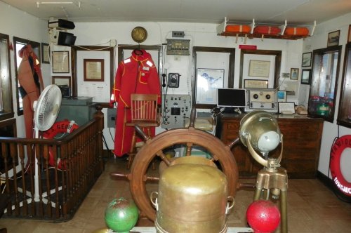 Interior of a vintage maritime room featuring a ship's wheel, equipment, and nautical decor.
