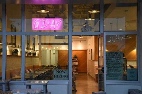 A restaurant entrance with a neon "G'DAY" sign, "NOW HIRING" notice, and a cozy interior visible through the windows.