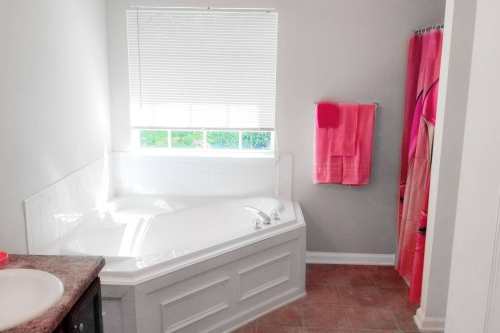 Bright bathroom featuring a corner bathtub, pink towels, and a shower curtain, with natural light from a window.