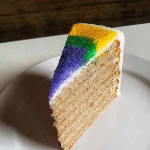 A slice of cake with layers, topped with colorful sprinkles in purple, green, and yellow on a white plate.