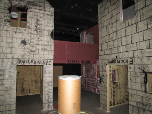Interior of a themed space with graffiti-style labels: "Eagles Nest 1," "Skyway Bridge," and "Barracks 3."