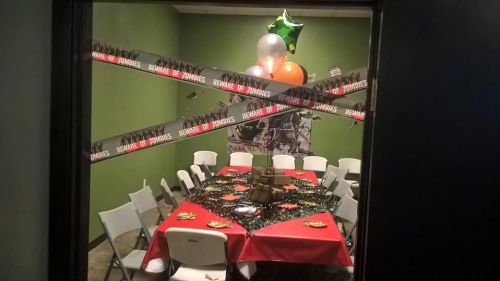 A decorated room with a zombie theme, featuring a table with snacks, balloons, and caution tape on the walls.
