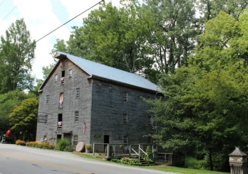 A rustic wooden barn surrounded by trees, with a metal roof and American flags displayed.