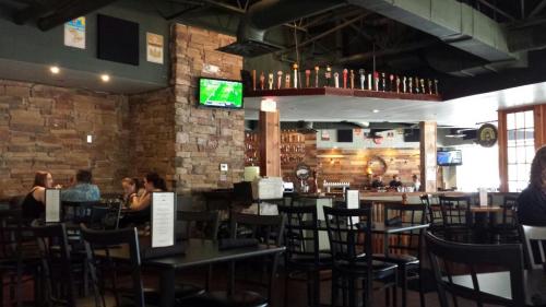 Interior of a restaurant with stone walls, a bar with taps, and patrons seated at tables. TVs are mounted on the walls.