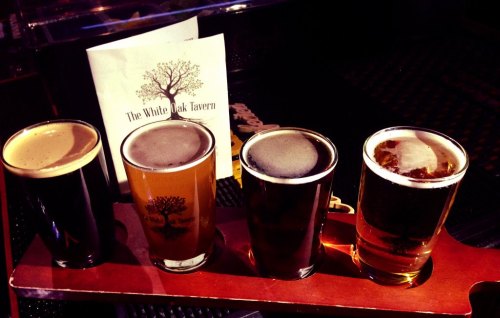 Four glasses of beer in a flight, with a menu from The White Oak Tavern in the background.