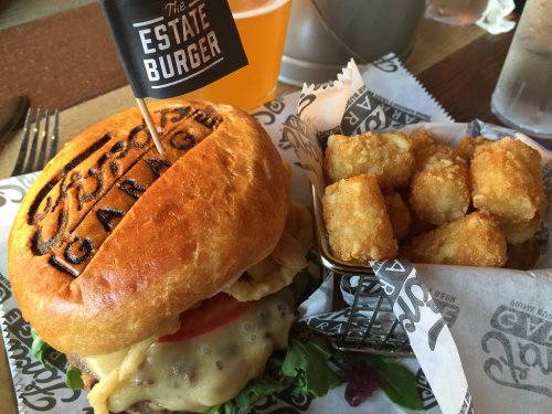 A gourmet burger with a toasted bun, lettuce, tomato, and cheese, served with a side of crispy tater tots.