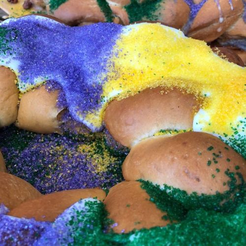 A colorful king cake decorated with purple, green, and yellow sugar, showcasing a festive design.