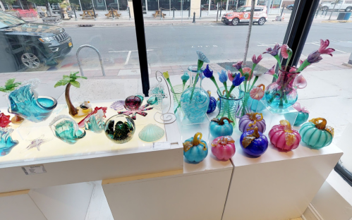 Colorful glass art pieces displayed in a shop window, including vases, pumpkins, and decorative shells.