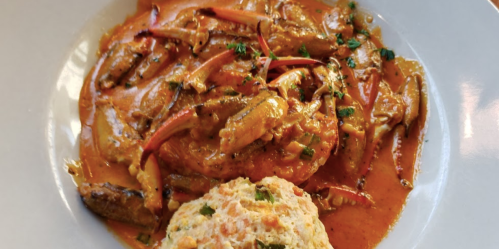 A plate of creamy shrimp dish with red peppers, served alongside a fluffy biscuit.
