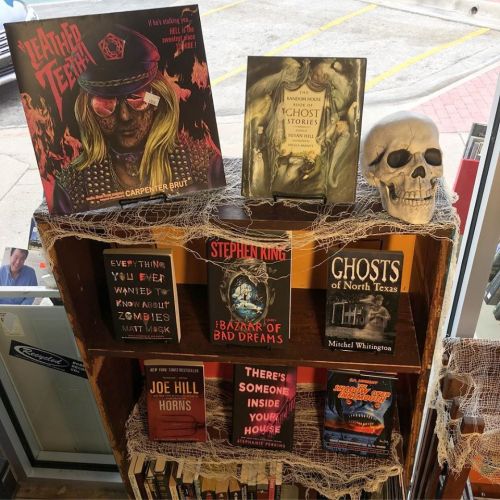 A wooden bookshelf displays horror-themed books, a skull, and spiderweb decorations, creating a spooky atmosphere.
