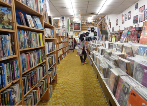 A cozy bookstore aisle lined with bookshelves and vinyl records, with a person browsing among the displays.