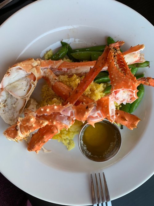 A plate featuring crab legs, yellow rice, green beans, and a small cup of melted butter.