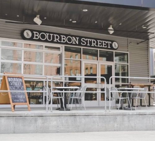 Exterior of a restaurant named "Bourbon Street," featuring outdoor seating and a sign advertising fresh food.