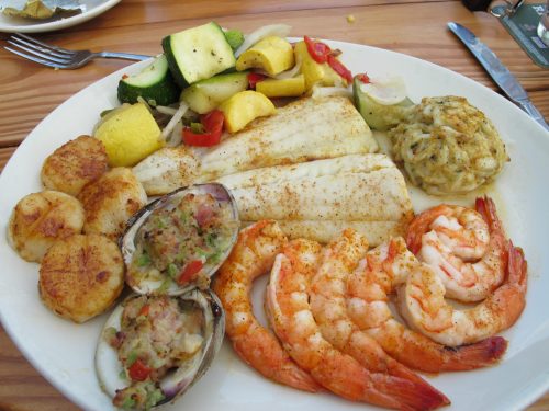 A plate of seafood featuring shrimp, fish fillets, stuffed clams, and sautéed vegetables.