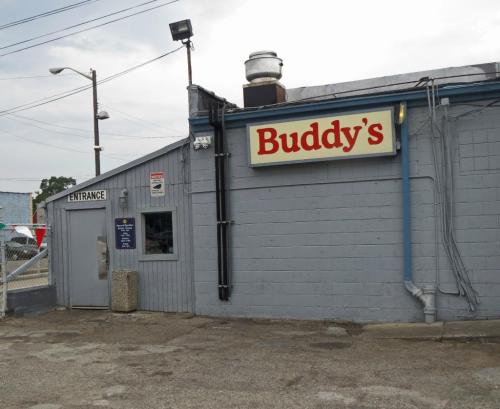 Exterior of Buddy's restaurant, featuring a sign and entrance, with a gray building and cloudy sky.