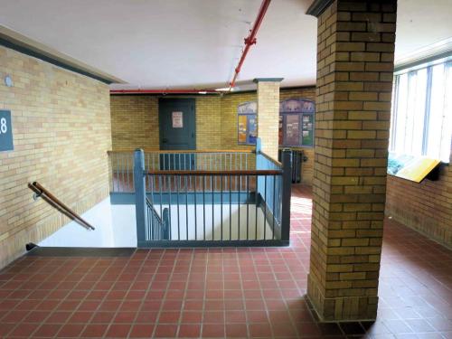 Interior view of a brick hallway with a staircase, railing, and windows, featuring a sign on the wall.
