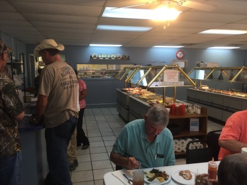 A casual dining area with a buffet, patrons enjoying food, and a man in a cowboy hat at the counter.