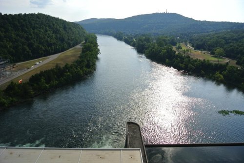 A serene river flows through a lush green landscape, reflecting sunlight under a clear sky.