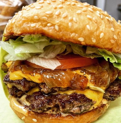 A close-up of a juicy cheeseburger with lettuce, tomato, and grilled onions on a sesame seed bun.