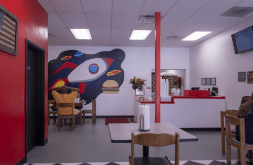 A colorful diner interior featuring a rocket mural, tables, and a counter with a staff member in the background.