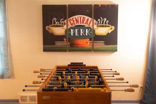 A foosball table in front of a Central Perk-themed wall art featuring coffee cups and the café's logo.