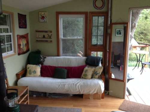 Cozy interior with a futon, decorative pillows, artwork on the walls, and a view of a deck through the windows.