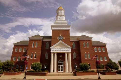 Exterior view of the Taylor County Justice Center, featuring a clock tower and American flags, under a cloudy sky.