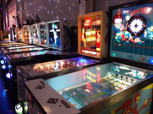 A row of vintage pinball machines illuminated in a dimly lit arcade, showcasing colorful designs and lights.