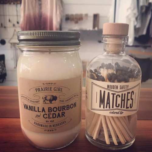 A jar of vanilla bourbon and cedar candle next to a bottle of colored safety matches on a wooden surface.