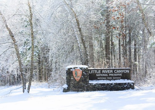 Sign for Little River Canyon National Preserve surrounded by snow-covered trees in a winter landscape.