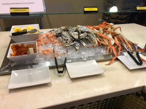 A seafood display featuring shrimp, oysters, crab legs, lemon wedges, and cocktail sauce on ice.