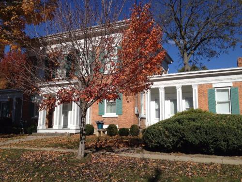 A brick house with white columns, surrounded by autumn trees and fallen leaves under a clear blue sky.