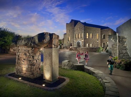 A stone archway leads to a building at dusk, with two girls in pink dresses and a man in traditional attire nearby.