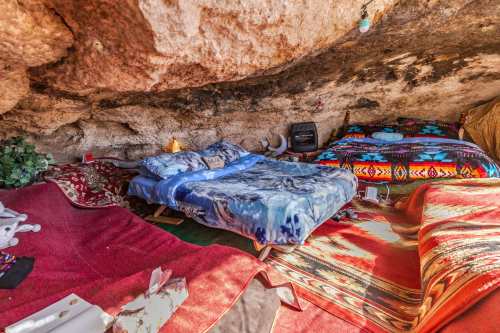 Cozy cave interior with colorful bedding, rugs, and a warm atmosphere, featuring two beds and decorative elements.
